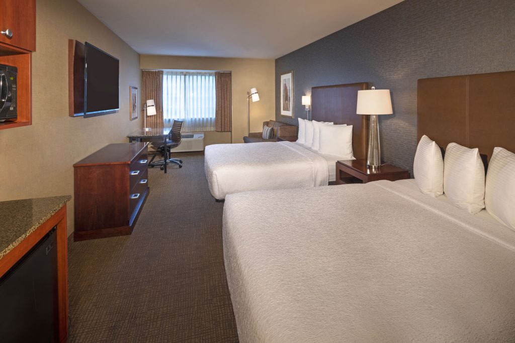 View of Silver Cloud Hotel - Portland hotel room with two queen beds with white bedding, dresser, desk, couch, and window